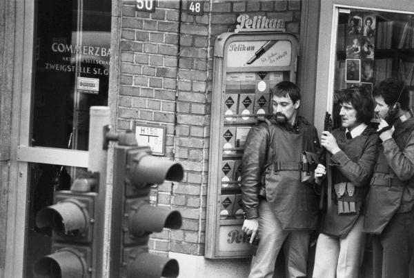 Bild 1 von 2: Am 18. April 1974 kommt es in der Commerzbank am Hamburger Steindamm zu einem Banküberfall mit anschließender Geiselnahme. Im Eingangsbereich des neben der Bank gelegenen Buch- und Schreibwarengeschäftes warten drei Angehörige des Mobilen Einsatzkommandos (MEK) mit Schutzwesten, Funkgerät, Pistole und Maschinenpistole auf ihren Einsatz.