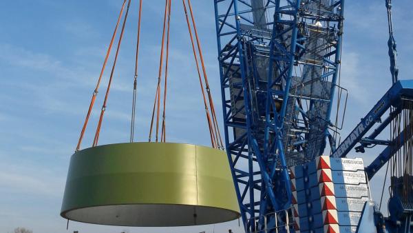 Bild 1 von 3: Ein Kran setzt das erste Turmsegment des Windrades auf das vorbereitete Fundament.