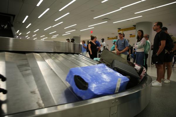 Bild 1 von 9: Passengers stand around a luggage carousel at the baggage claim in the John F. Kennedy International Airport.
