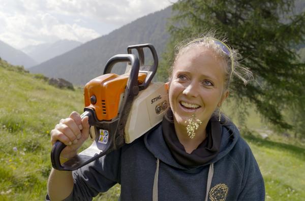 Bild 1 von 4: Holzbildhauerin Nora Engels läuft mit Motorsäge auf der Schulter einen Berghang im Oberengadin hinauf.