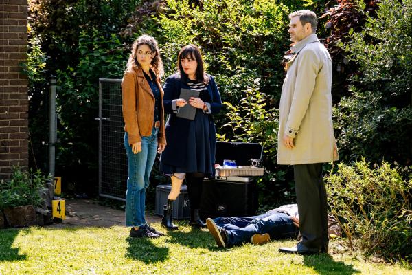 Bild 1 von 6: Ein Jahr nach seinem angeblichen Tod wird Tom Gerdes (Komparse, liegend) erschlagen im Garten seiner Frau aufgefunden. Kommissare Lilly Funke (Tatjana Kästel, l.) und Jonas Fischer (Lukas Piloty, r.), sowie Rechtsmedizinerin Dr. Pilar Westphal (Yulia Yáñez Schmidt, M.) fragen sich, wie es zu diesem doppelten Tod kommen konnte. (Komparse im Bild)