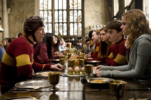 Bild 1 von 15: Rupert Grint as Ron Weasley wearing helmet and Quidditch uniform, seated at table in Great Hall talking with Bonnie Wright as Ginny Weasley, Daniel Radcliffe as Harry Potter, and Emma Watson as Hermione Granger.
