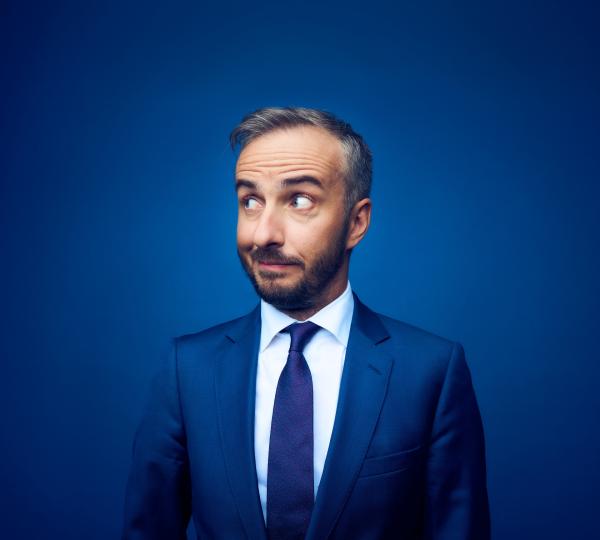 Bild 1 von 1: Jan Böhmermann im blauen Anzug vor blauem Hintergrund.