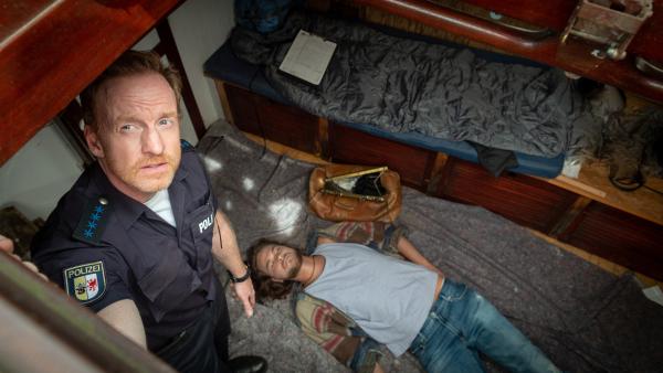 Bild 1 von 7: Niklas Norberg (Jonathan Rickelt, r.) liegt leblos in der Kajüte eines Bootes. Offenbar hat der Junge in dem Boot gelebt, wie Timmermann (Mathias Junge, l.) seinen Kollegen berichtet. Ersten Ermittlungen nach hat der junge Mann sein Abitur abgebrochen und dem bürgerlichen Leben den Rücken gekehrt. Aber warum hat er sich für ein Leben als Aussteiger entschieden? Was ist passiert? Hängen der Mord an ihm und seine Flucht aus der Gesellschaft zusammen?