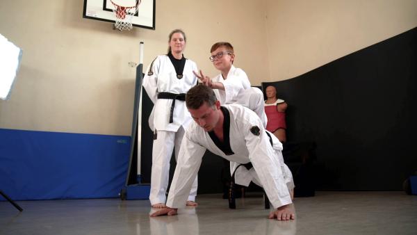 Bild 1 von 4: Bei diesem Prank wird Taekwondo-Trainer Nils (M.) an seine Grenzen gebracht. Los geht es mit Liegestützen, erschwert durch den 9-jährigen Taylan (r.), der fröhlich auf seinem Rücken sitzt. Trainerin Pia (l.) ist gespannt.© ZDF/Contentladen - Honorarfreie Verwendung gemäß AGB im redaktionellen Zusammenhang mit genannter Sendung bei Nennung \