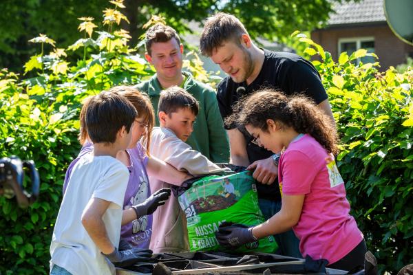 Bild 1 von 8: Kinder der Wilhelm-Lehmbruck Grundschule im Schulgarten an einem Hochbeet zusammen mit Gärtnern.