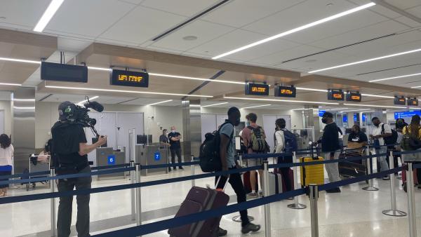 Bild 1 von 8: A cameraman is focused on various passengers as they wait in line with their luggage.