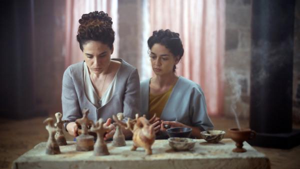 Bild 1 von 7: Pimanara (Sofia Kikilintzi) und Sijama (Rania Athanasopoulou) vollziehen ein Ritual zu Ehren der Göttinnen. Die minoische Religion umfasste die Verehrung von Naturgottheiten, die Durchführung von Ritualen sowie die Darbringung von Opfergaben wie Lehmfiguren und Feldfrüchten.