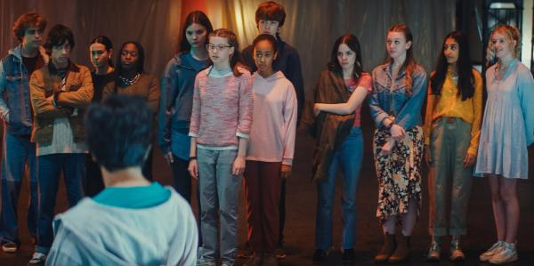 Bild 1 von 5: Die Erdrutsch-Gruppe mit Kai (Charlie Banks), Jay (Noah Manzoor), Dev (Kalli Tant) und Meena (Florisa Kamara), die Control-Alt-Gruppe mit Isabel (Alis Waters), Monika (Lucy Chambers), Faye (Keira Chansa) und Luka (Pádraig McCormack) sowie die Phönix-Gruppe mit Emma (Emily Flain), Maeve (Skye McClenaghan), Yasmin (Maariya Razzaq) und Carrie (Ellen Taylor, hinten - v.l.n.r.) betrachten die Neuankömmlinge, die Libellen-Gruppe mit Glen (Krish Misra, v.).