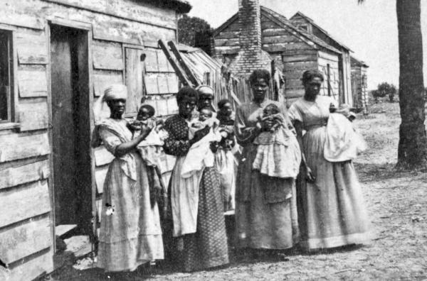 Bild 1 von 3: Versklavte Menschen vor ihren Wohnquartieren auf der Plantage T.J. Fripp, auf der Insel St. Helena, South Carolina