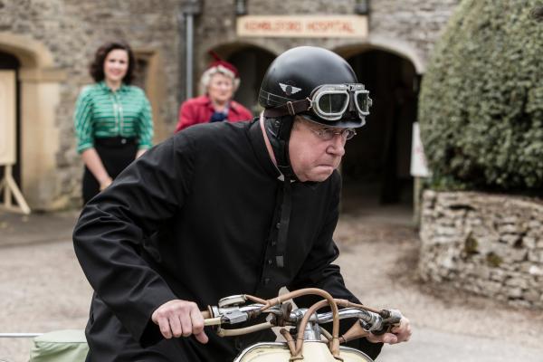Bild 1 von 6: Father Brown (Mark Williams, r.) will um jeden Preis die Wahrheit rausfinden, bevor es zu spät ist. Dafür wagt er sich sogar auf den Motorroller und lässt seinen Drahtesel stehen. Mrs. McCarthy (Sorcha Cusack, M.) und Bunty (Emer Kenny, l.) können nur noch hoffen, dass er sich nicht verletzt.