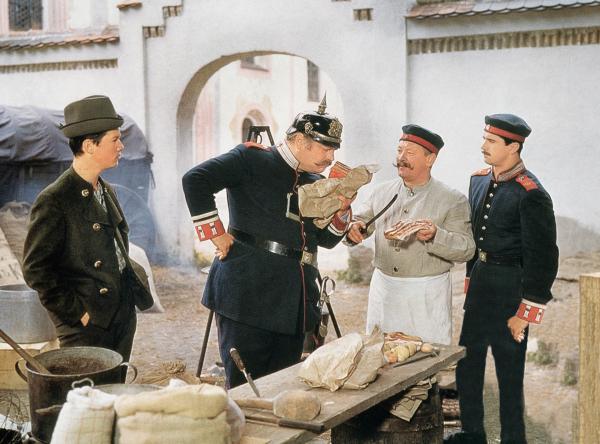 Bild 1 von 2: Feldwebel Falkenberg (Rudolf Rhomberg, 2. von links) kontrolliert die Erbsensuppe mit Speck, die der Kompaniekoch (Tschik Cajkovski) zubereitet. Lausbub Ludwig (Hansi Kraus, links) will dem ungehobelten Spieß eine Lektion erteilen.