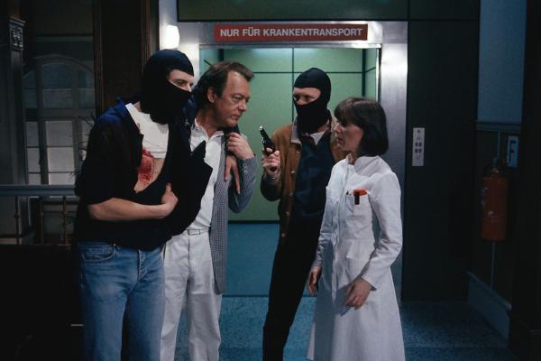 Bild 1 von 2: Mattes (Arthur Brauss, 2. v. r.) zwingt Professor Brinkmann (Klausjürgen Wussow, 2. v. l.) und Dr. Elena Bach (Heidelinde Weis, r.) dazu, seinen angeschossenen Komplizen (Udo Wachtveitl, l.) zu operieren.