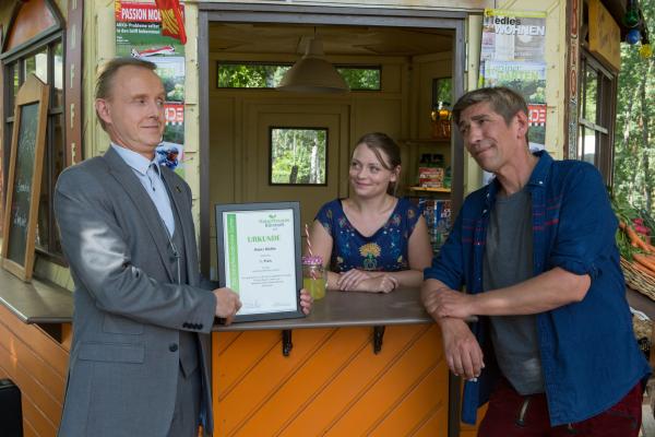 Bild 1 von 7: Ausgerechnet Herr Kluthe (Holger Handtke, l.) will den Kampf gegen Fritz (Guido Hammesfahr, r.) um den naturfreundlichsten Garten Bärstadts gewinnen. Charlie (Géraldine Raths, M.) steht im Kiosk und lächelt.