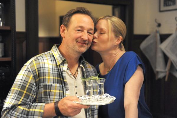 Bild 1 von 6: Gregor (Holger Matthias Wilhelm) hat zwei Schnäpse für ein älteres Paar vorbereitet, die sich in Lansing das Ja-Wort geben wollen, als Vera (Sybille Waury) runter kommt und ihm einen Kuss auf die Wange gibt.