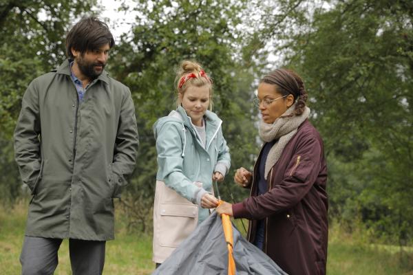 Bild 1 von 4: Yaa (Rebecca Lina, r.) regt sich vor Paula (Maike Jüttendonk, M.) über ihren Mann auf, als Jannos (Jasin Challah, l.) vorbeikommt, um sie zu begrüßen.