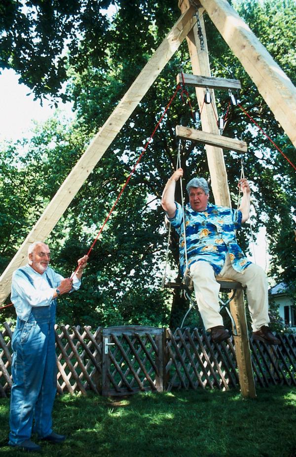 Bild 1 von 3: Peter (Peter Lustig, l.) hat einen Flaschenzug konstruiert. Sein kräftig gebauter Nachbar Paschulke (Helmut Krauss, r.) dient ihm als Testobjekt.