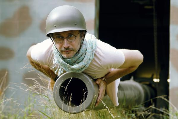 Bild 1 von 7: Portrait von Michael Ostrowski mit Stahlhelm auf dem Kopf auf einer Kanone liegend im Bunkermuseum während ServusTVs \