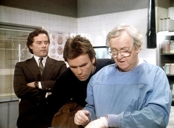Bild 1 von 10: Bannister (Michael W. Goodwin, l.) und MacGyver (Richard Dean Anderson, M.) beobachten, wie der Pathologe (Arthur Malet, r.) eine Gewebeprobe entnimmt.