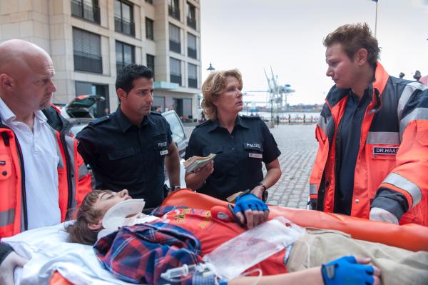 Bild 1 von 14: Ein Geldumschlag des verunglückten Rollstuhlfahrers Kristof (Joel Eisenblätter, liegend) lässt Tarik (Serhat Cokgezen, 2v.l.) und Claudia (Janette Rauch, 2.v.r.) aufhorchen. Doch Notarzt Haase (Fabian Harloff, r.) kann ihnen nicht weiterhelfen.