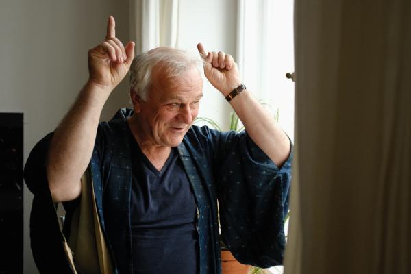 Bild 1 von 2: Dieter (Bernhard Schütz) lässt sich die Laune durch die Quarantäne nicht verderben. Er flirtet am Fenster mit einer Nachbarin.
