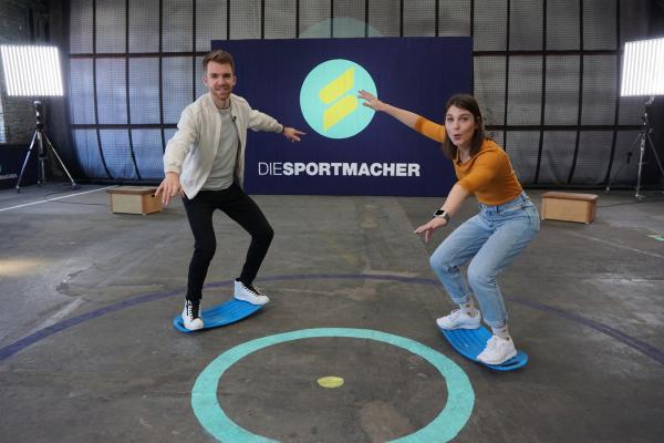 Bild 1 von 7: Das Moderatorenteam Laura und Stefan machen Trockenübungen für's Windsurfen, um ihre Balance zu trainieren. Keine leichte Aufgabe!