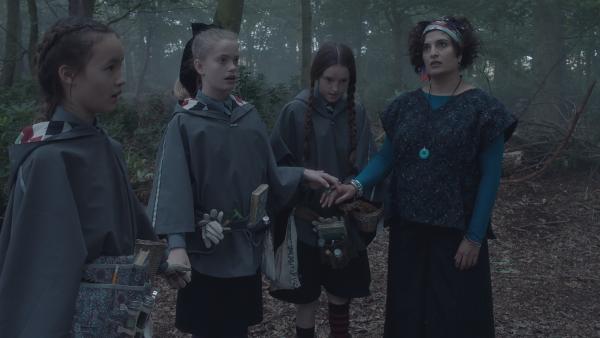 Bild 1 von 6: Nacheinander verfallen Felicitas (Dagny Rollins, l.), Esther (Jenny Richardson, 2. v. l.) und Frau Schimmel (Mina Anwar, r.) in einen tranceähnlichen Zustand. Ob das als ausgestorben geltende gefährliche Wesen doch noch in dem Wald lebt? Mildred (Bella Ramsey, 3. v .l) sucht nach einem Mittel, die drei zu erlösen.