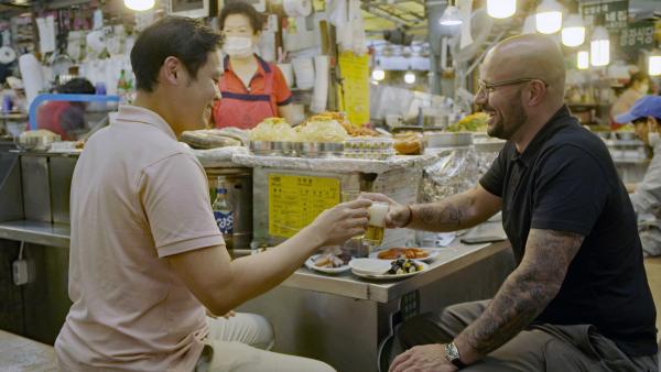 Bild 1 von 6: Auf dem Gwangjang-Markt in Seoul probieren sich Carlton McCoy (r.) und Kyungmoon Kim (l.) durch verschiedene Speisen und Getränke.