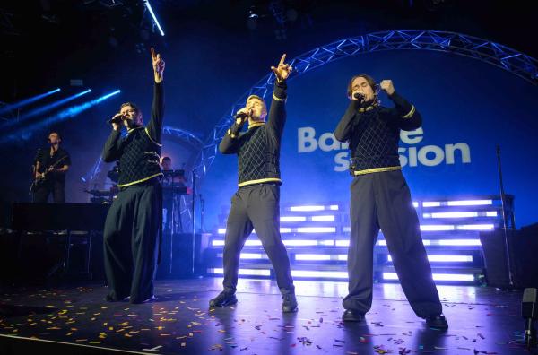 Bild 1 von 2: Gary Barlow (2.v.r.), Mark Owen (re.) und Howard Donald (2.v.l.) nehmen das Publikum mit auf eine humorvolle und selbstironische Reise durch die Bandgeschichte.