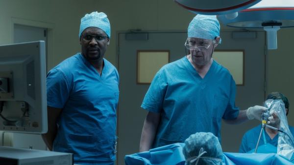 Bild 1 von 3: Als der Oberarzt Mr. Lockhart (Alex Jennings, r.) erfährt, dass eine Patientin entgegen seiner Anweisung operiert wird, sind er und sein Assistent Julian (Kadiff Kirwan, l.) bereit, die Aktion zu beenden. Doch dann machen die beiden eine Entdeckung, die alles verändert.