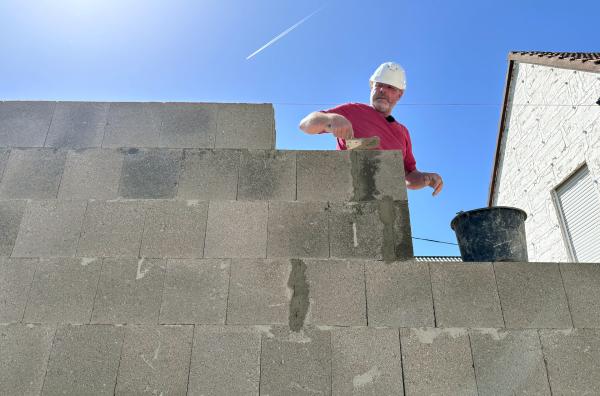 Bild 1 von 4: Maurer Daniel Marques beim Mauern des Erdgeschosses mit Bimssteinen.