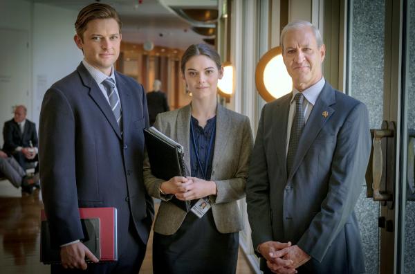 Bild 1 von 4: Minister Kevin Cartwright (David Roberts, re.), unterstützt von Christopher (James Sweeny, li.) und Daphne (Rose Riley, Mi.), hadert mit dem neuen Gesetzentwurf von Alex und scheint im letzten Moment einen Rückzieher machen zu wollen.