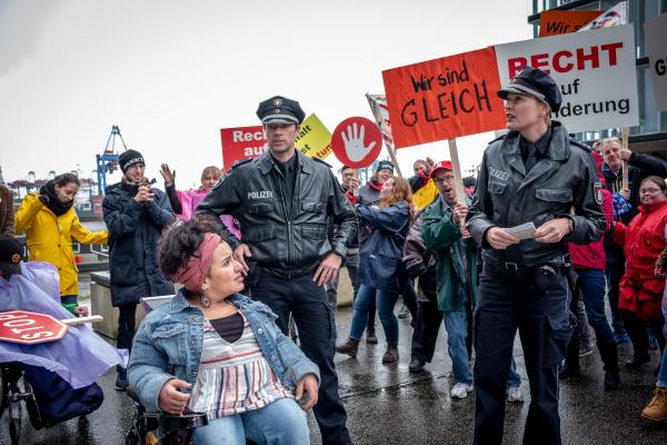 Bild 1 von 9: Melanie (Sanna Englund, r.) und Mattes (Matthias Schloo, 2.v.l.) müssen zu einer unangemeldeten Demo, die von der Aktivistin Cora Liberti (Kübra Sekin, l.) organisiert wurde. (Rest: Komparsen).