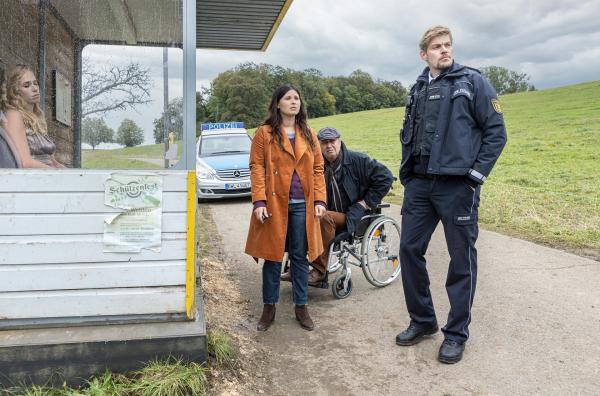 Bild 1 von 3: An einer Bushaltestelle ist die Leiche einer jungen Frau gefunden worden. Als örtliche Bestatter sind Lisa (Anna Fischer) und Alfons Taubenbaum (Artus Maria Matthiesen) vom Polizisten Andi Kuhn (Helgi Schmid) wegen des Abtransports gerufen worden. Allerdings ist die Identität der Toten nicht feststellbar, mit wem sollen die Taubenbaums über die Beerdigung reden?