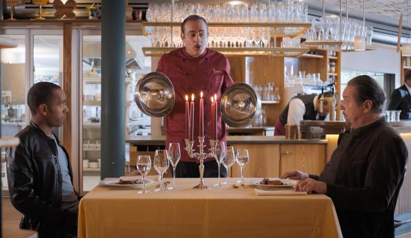 Bild 1 von 1: Beissl (Andreas Giebel, M.) und Jerry (Peter Marton, l.) werden im Restaurant Nouvelle Cuisine von Michelle Perrin (Miguel Abrantes Ostrowski, M.) persönlich bedient.