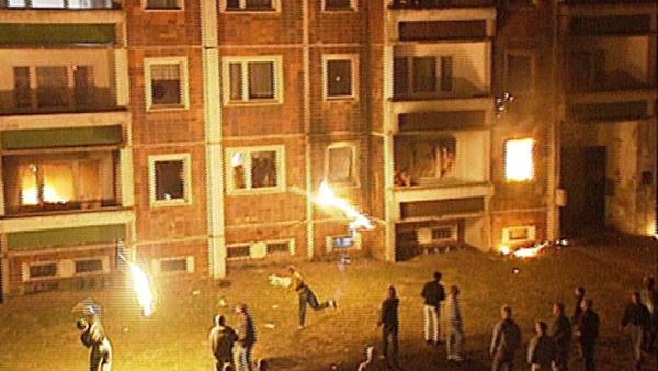 Bild 1 von 2: 1992 schleudern Rechtsextreme Brandsätze in die Wohnungen von ehemaligen Vertragsarbeitern in Rostock-Lichtenhagen. Die  Polizei verliert die Kontrolle, die Bevölkerung klatscht Beifall.
