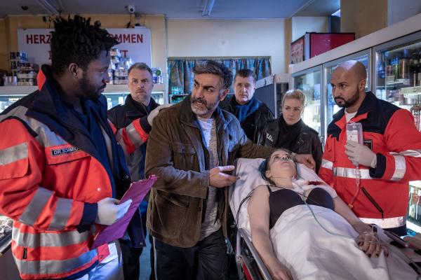 Bild 1 von 8: Bei dem Überfall auf Demir Kaplans (Neil Malik Abdullah, 3.v.l.) Laden wurde dessen Tochter Paula (Hannah Bortz) angeschossen. Während Dr. Schmidt (Joel Williams, l.) den aufgeregten Vater beruhigt, warten Sven Reimers (André Röhner, 2.v.l.), Hans (Bruno F. Apitz, M.) und Franzi (Rhea Harder-Vennewald) darauf, ihn befragen zu können.