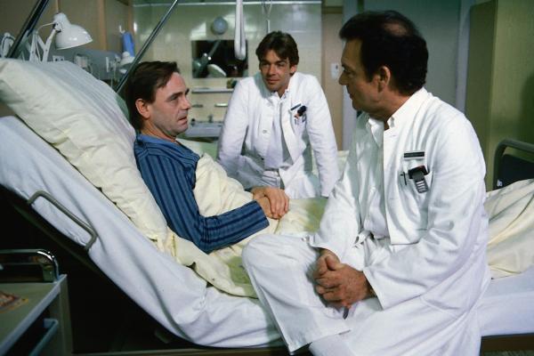 Bild 1 von 1: Dr. Rens (Holger Petzold, l.) ist plötzlich erkrankt. Er sieht einer Operation entgegen. Auch ein Arzt kann Angst vor einer Blinddarmoperation haben. Professor Brinkmann (Klausjürgen Wussow, r.) und sein Sohn Udo (Sascha Hehn, M.) versuchen ihm gut zuzusprechen.