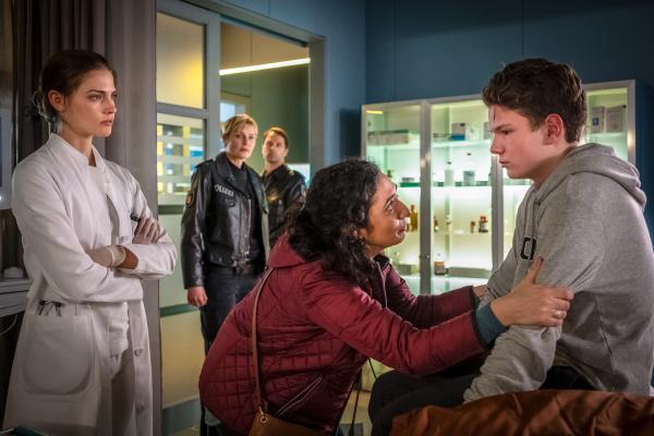 Bild 1 von 7: Dr. Eva Grünberg (Laura Berlin, l.) glaubt Ruth Grönhoffs (Ariella Hirshfeld, 2.v.r.) Geschichte zur Verletzung ihres Sohnes Emil (Julius Störmer, r.) nicht. Auch Melanie (Sanna Englund, 2.v.l.) und Mattes (Matthias Schloo, M.) wundern sich über das Verhalten von Frau Grönhoff.